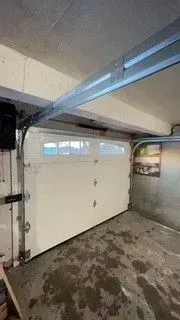 Empty garage with a white door, high ceiling, and a wet concrete floor.