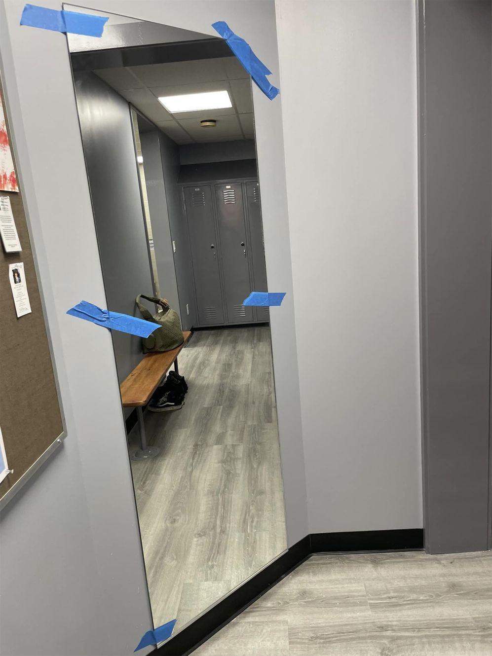 A full length mirror is taped to a wall in a hallway.