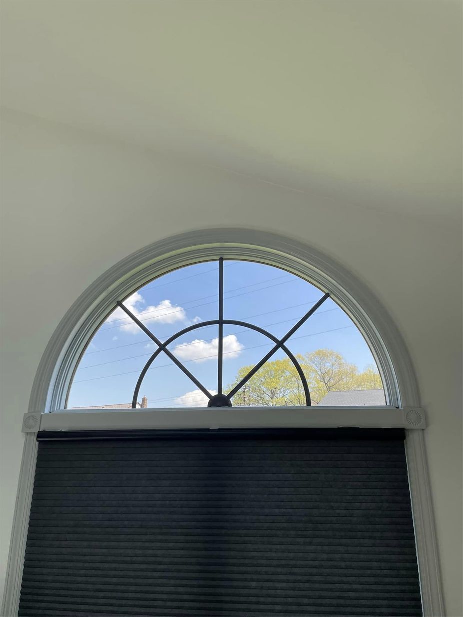 A large arched window with black blinds and a blue sky behind it.