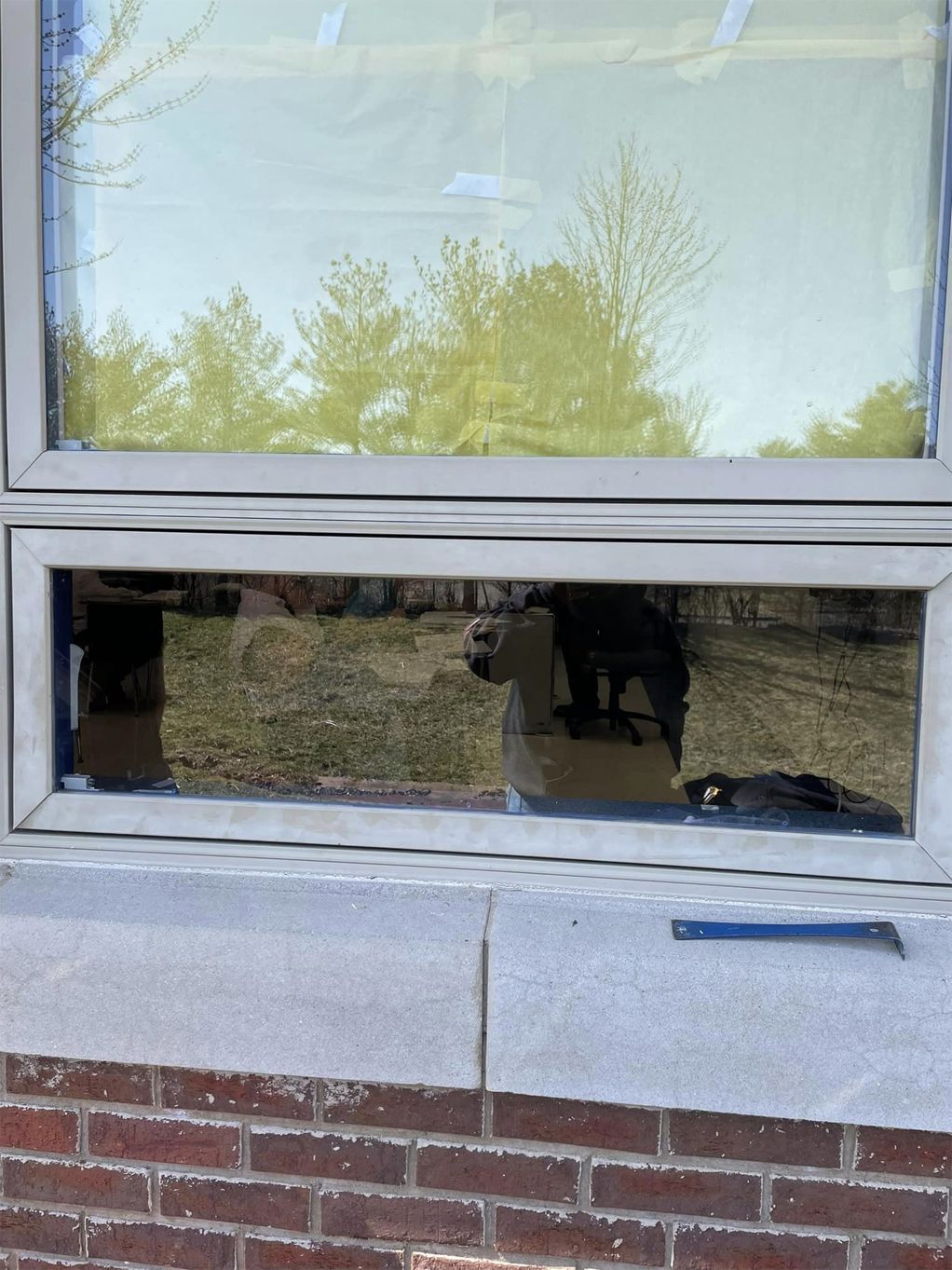 A window on a brick building with a reflection of trees in the window.