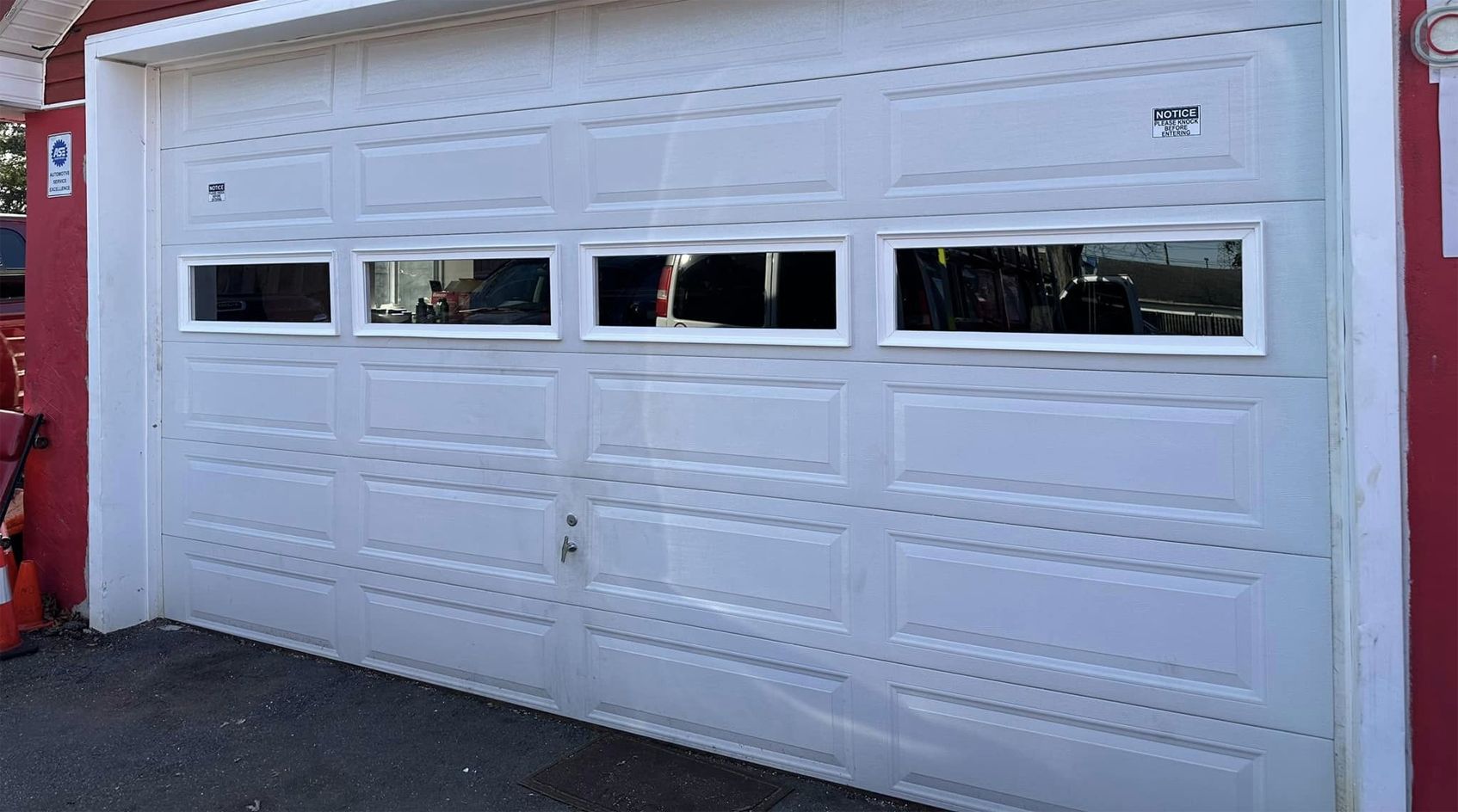 A white garage door with three windows and a red wall.