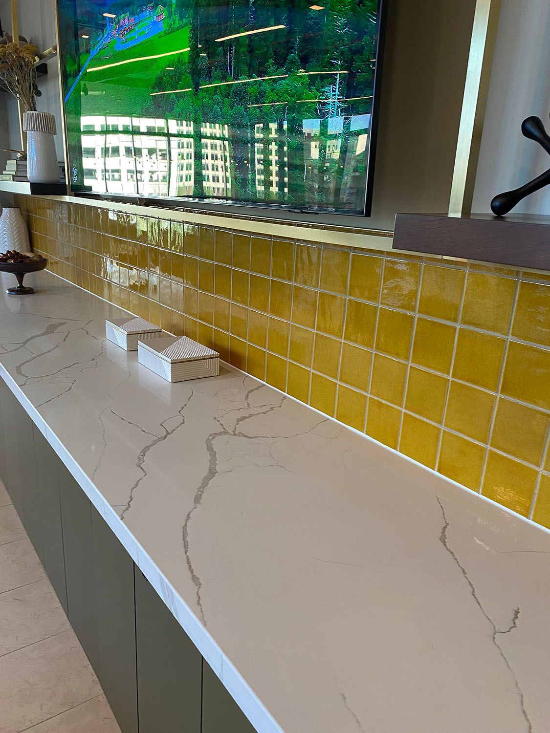 a counter with yellow backsplash tiles and a flat screen tv