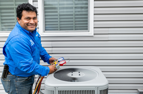 A man in a blue shirt is working on an air conditioner outside of a house