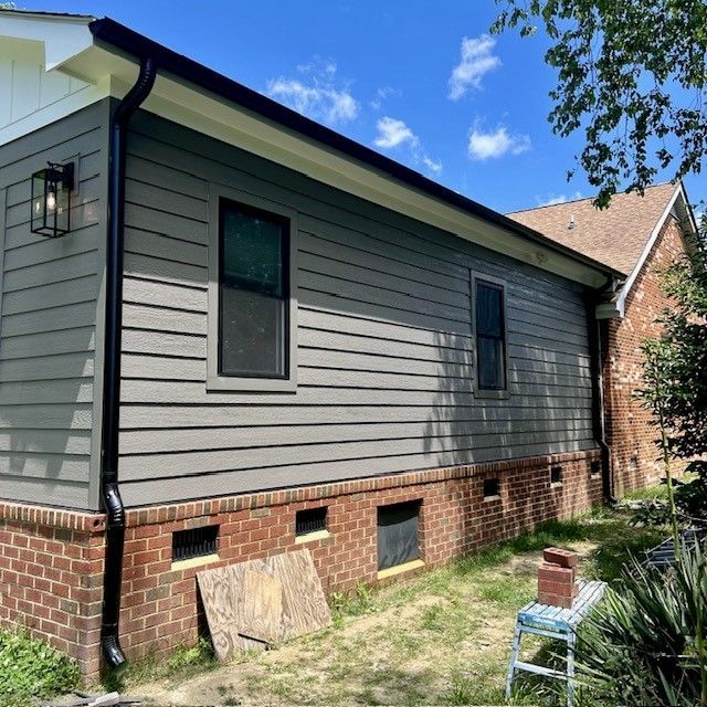 A brick house with a gray siding and a black gutter