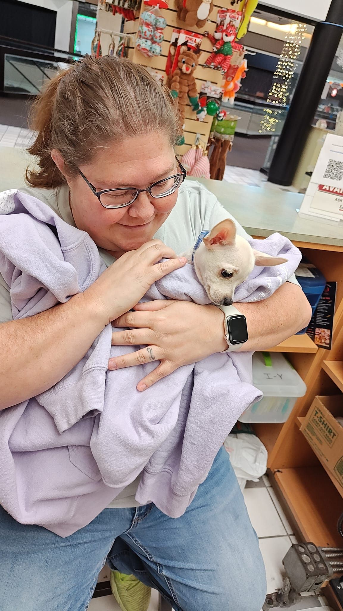 Person in a lavender sweater cuddling a small white rabbit in a shop aisle