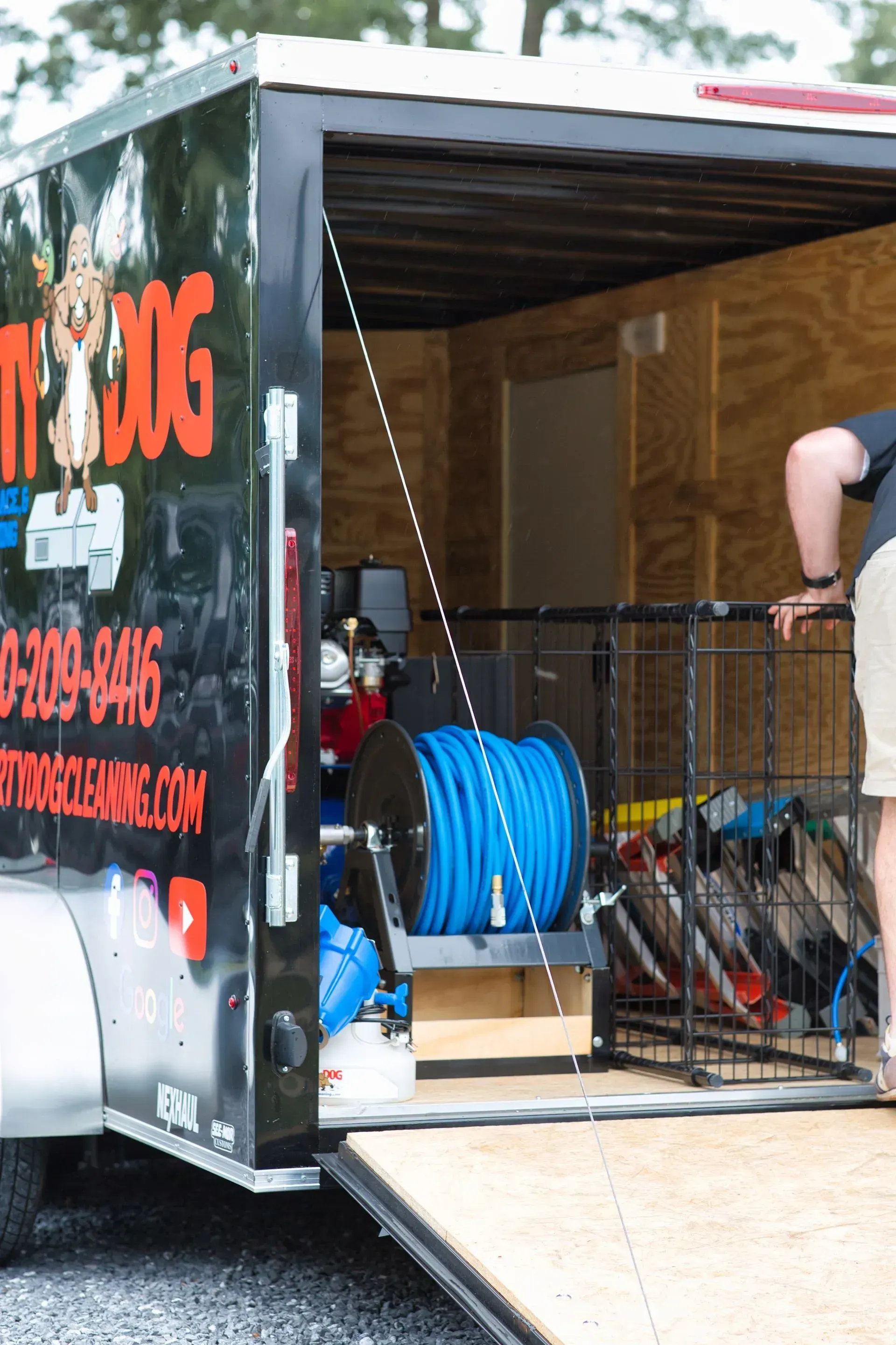 Open trailer with blue hose reel and equipment inside, ramp lowered to the ground