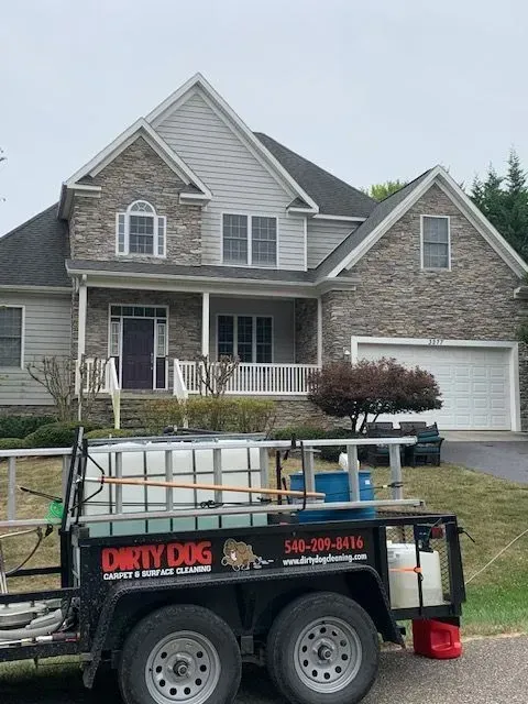 Roofing trailer in front of a stone house with a garage and porch.