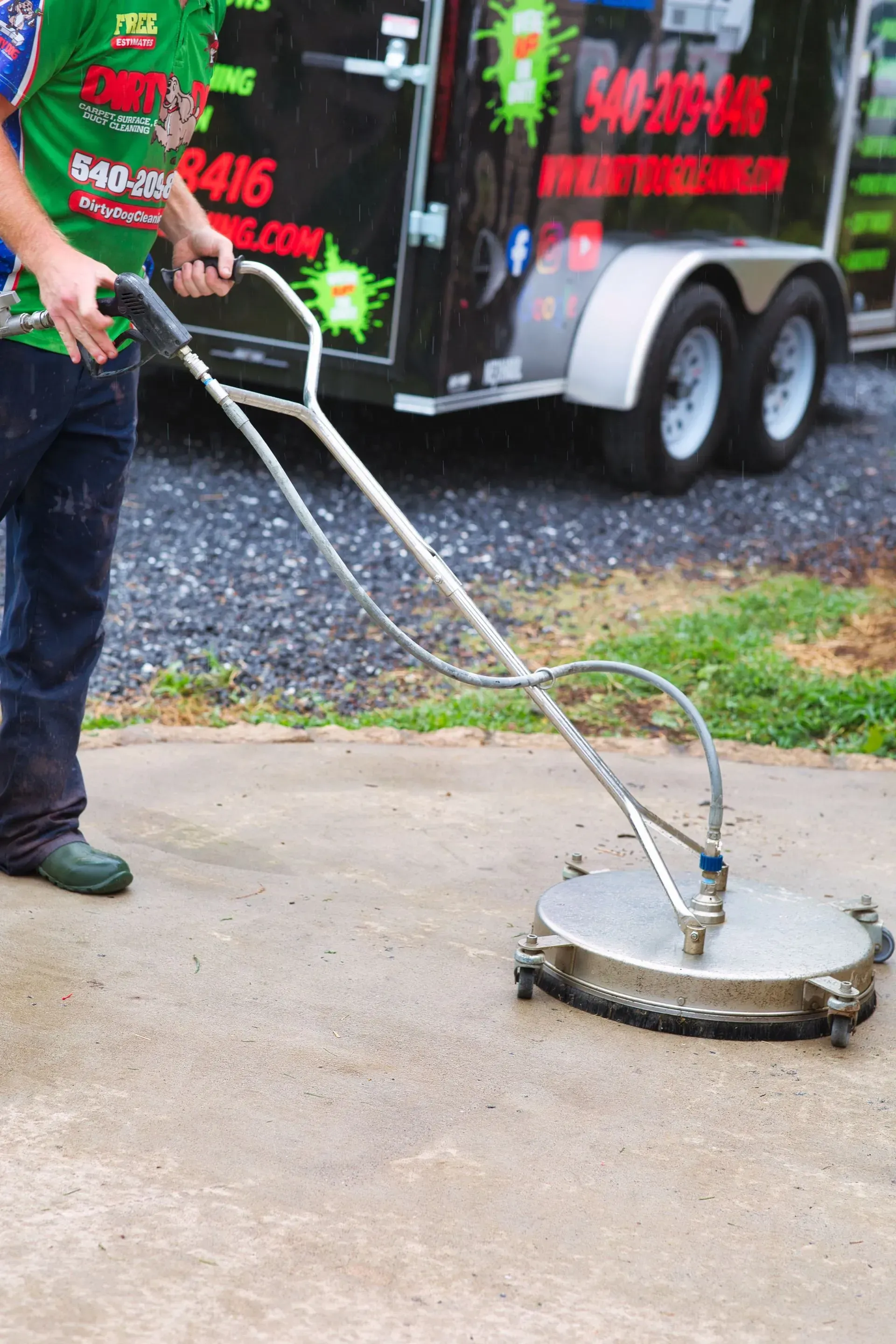 Person using a pressure washer to clean a concrete surface beside a trailer.