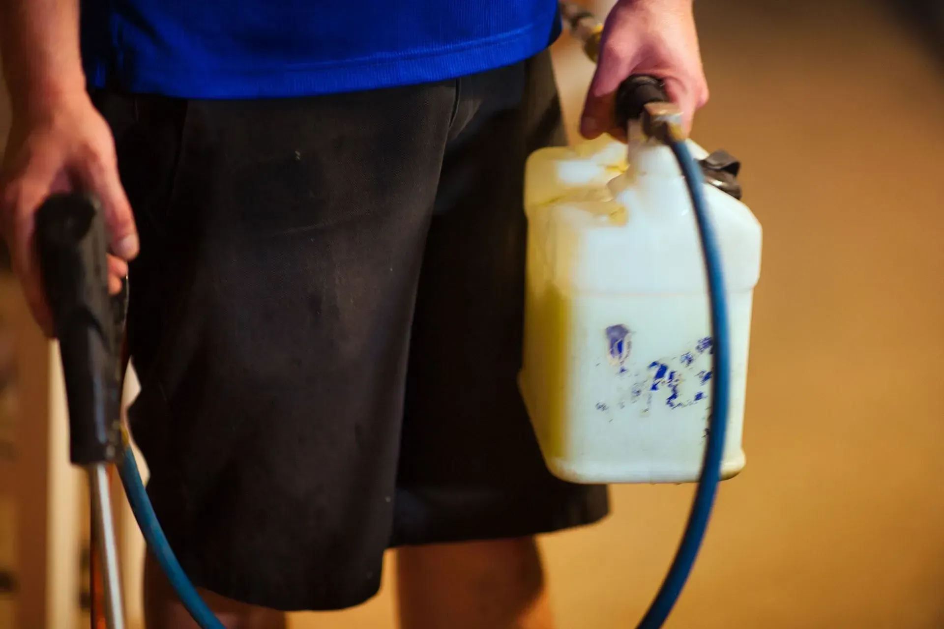 Person holding a white sprayer and blue hose against a warm indoor background