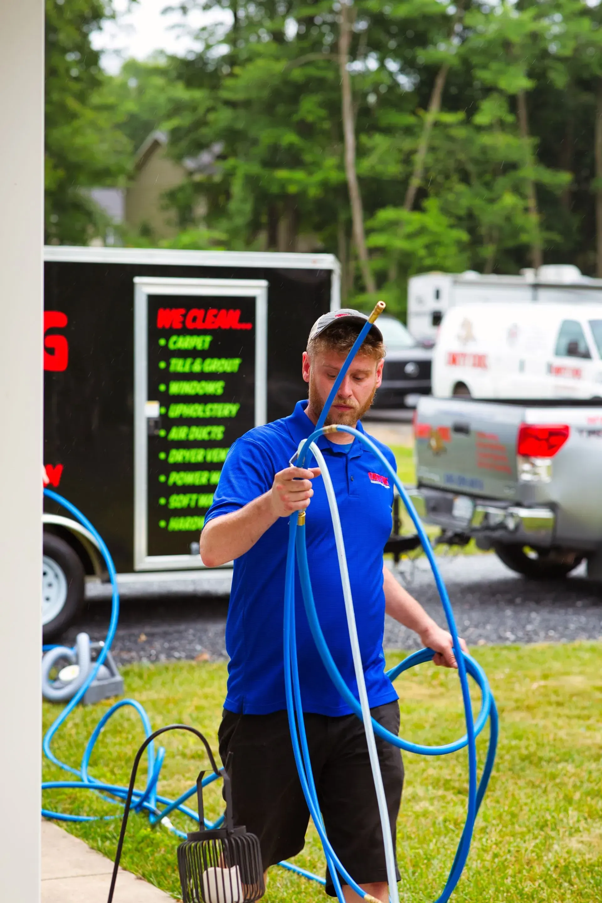 Man in blue shirt handling long blue hoses outdoors near a truck and equipment sign