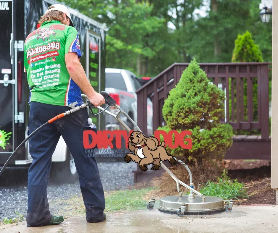 Worker in green shirt pressure-washes a sidewalk beside a driveway.
