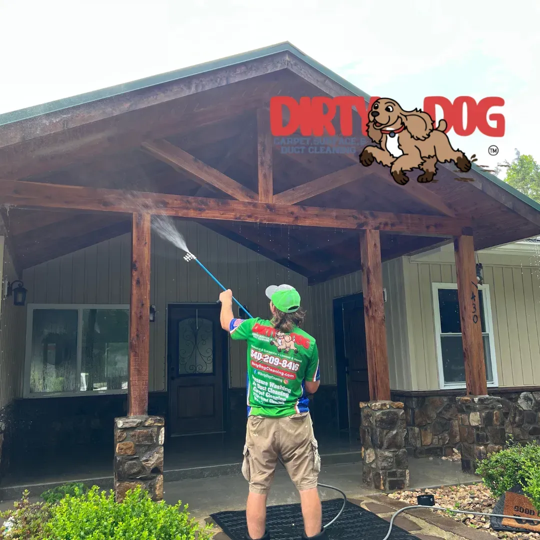 Worker pressure-washes the porch of a rustic cabin beneath a Dirty Dog logo sign.