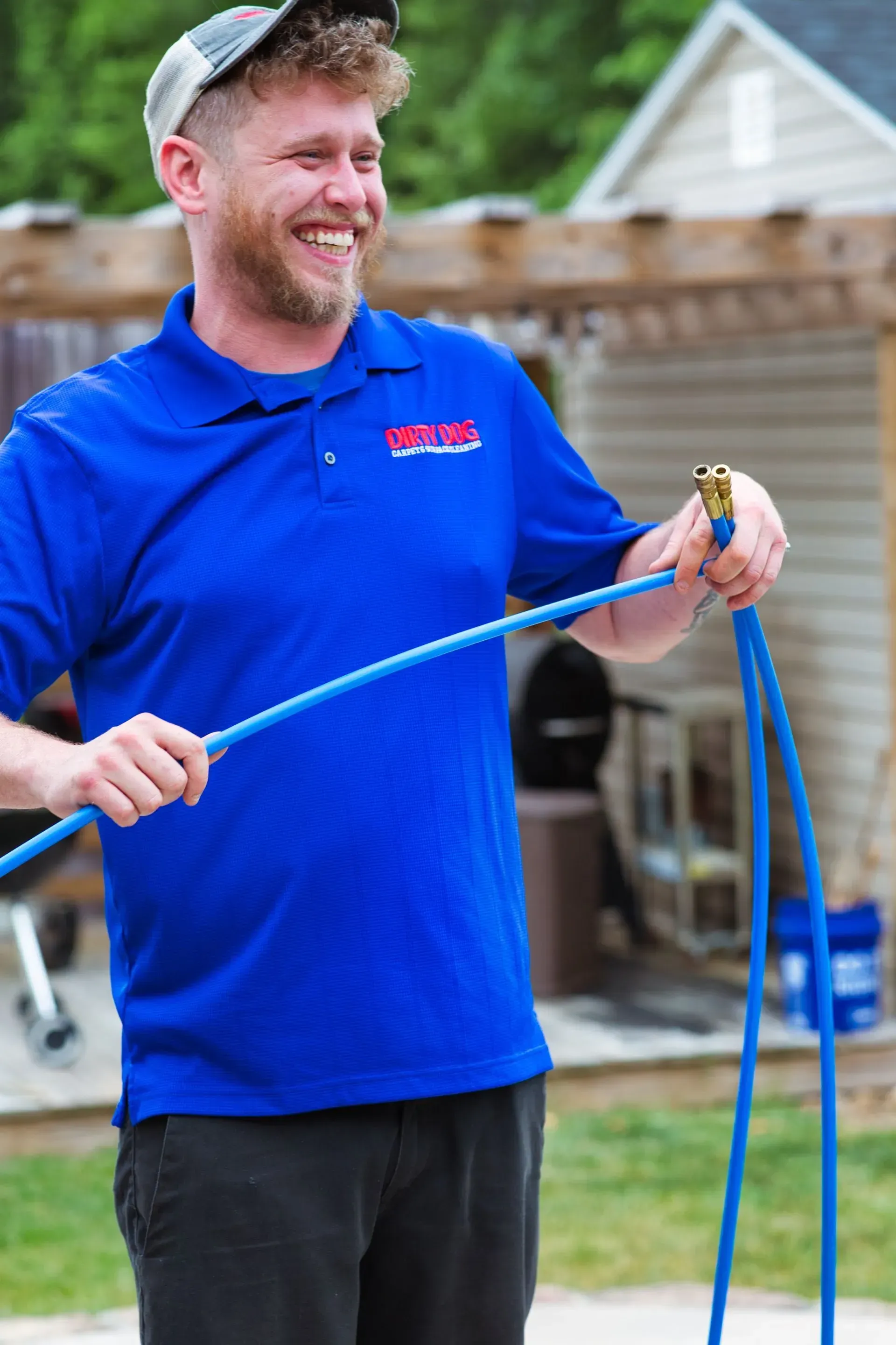 Man in a blue shirt holding a blue rope and smiling outdoors in a yard