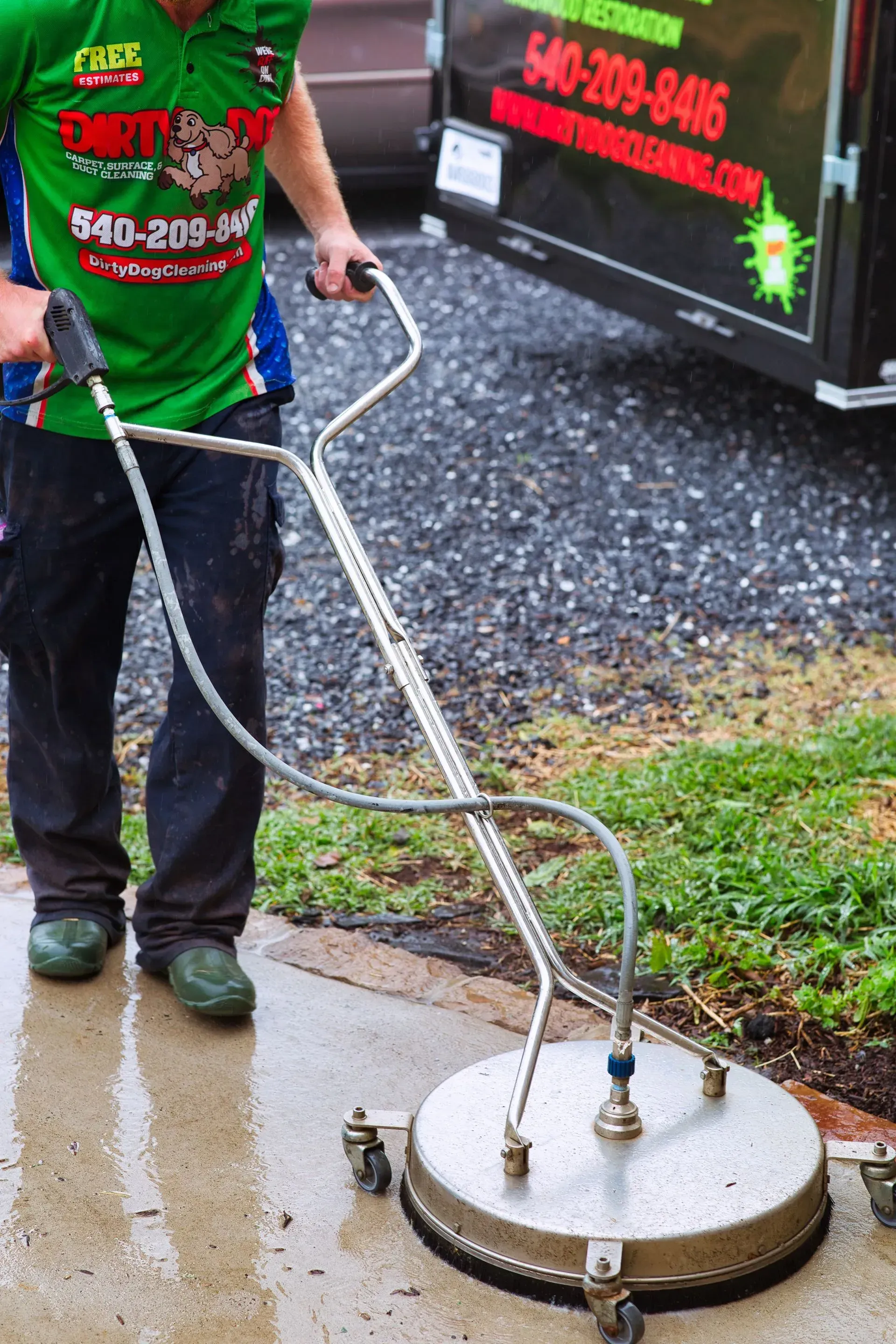 Worker using a surface cleaner to pressure wash a sidewalk beside a truck.