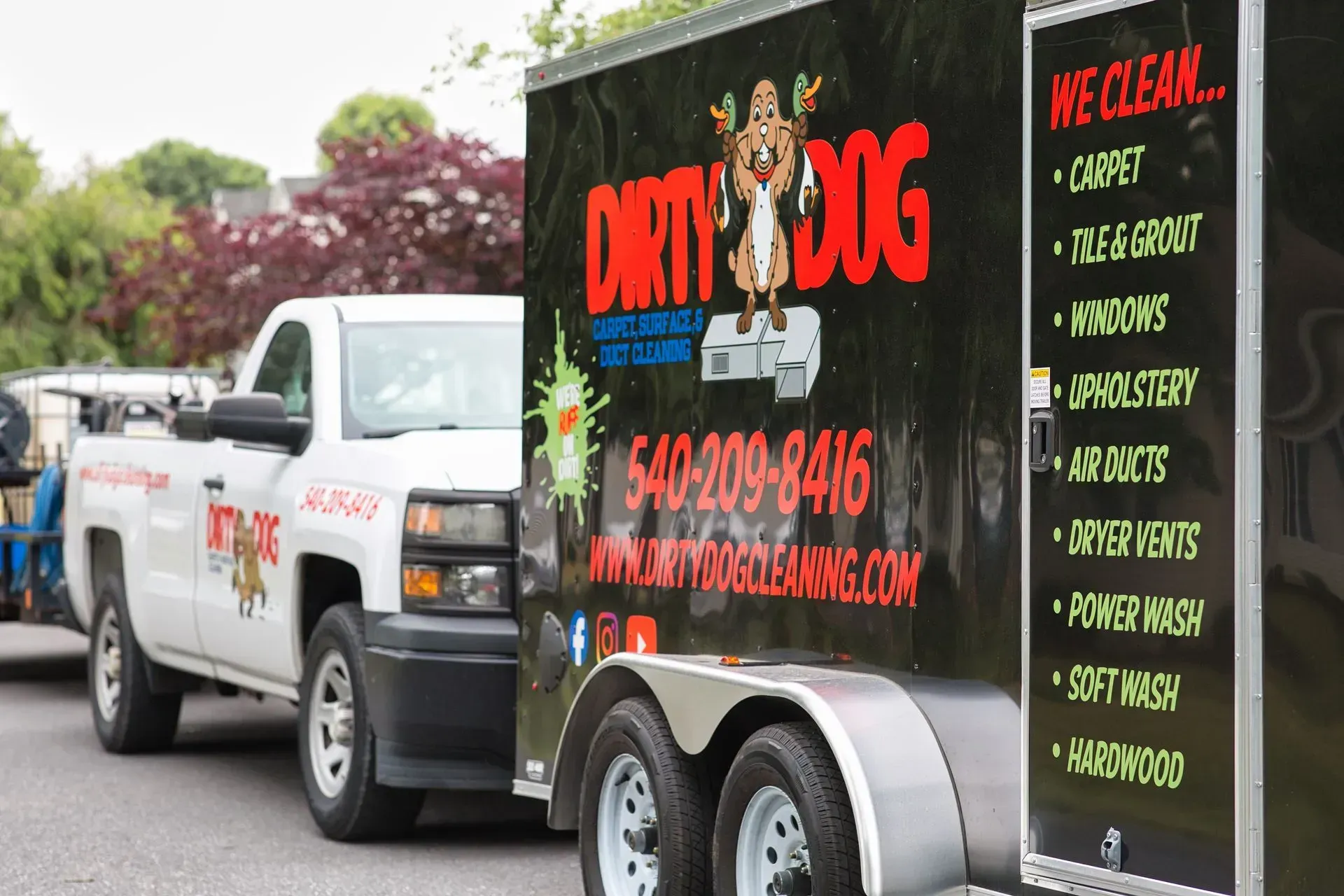 White truck towing a black dog grooming trailer with red lettering on a road outdoors