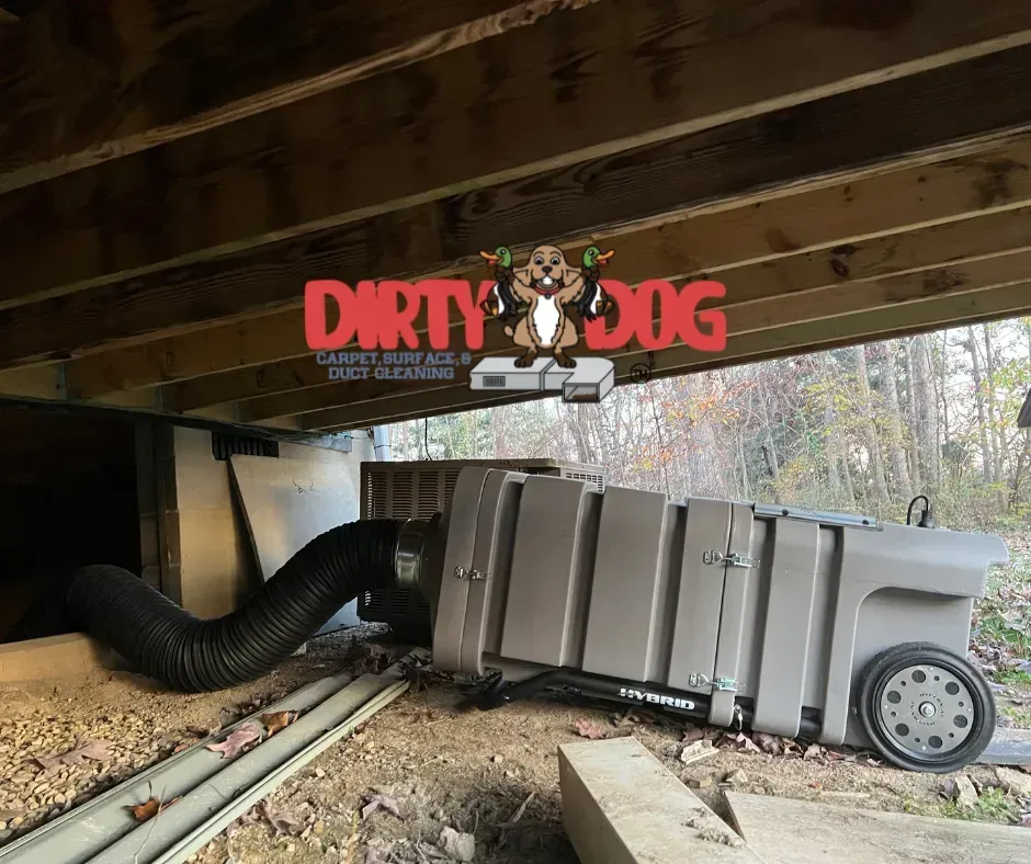 Collapsed gray utility trailer under a deck, with debris and a large black hose nearby.