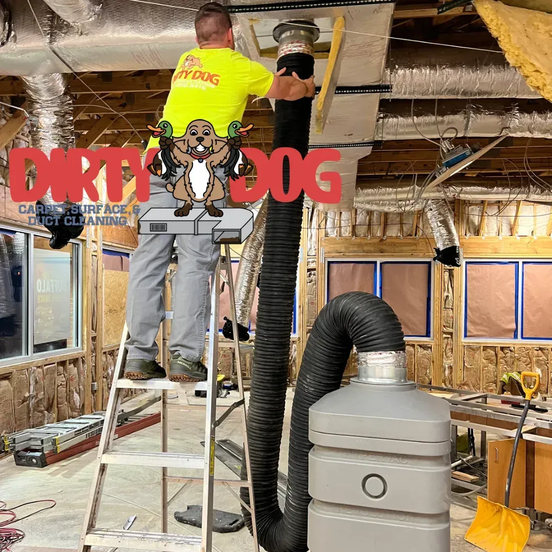 Worker on ladder installing black duct in unfinished attic with exposed insulation and HVAC equipment