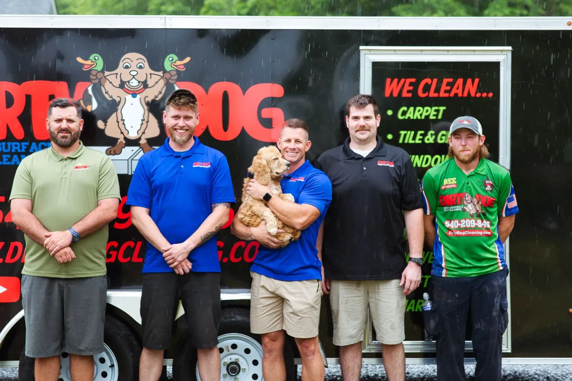 Five people posing in front of a black trailer with cleaning service signage.