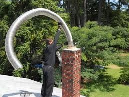 Man installing flexible metal chimney liner on a brick chimney on a roof.
