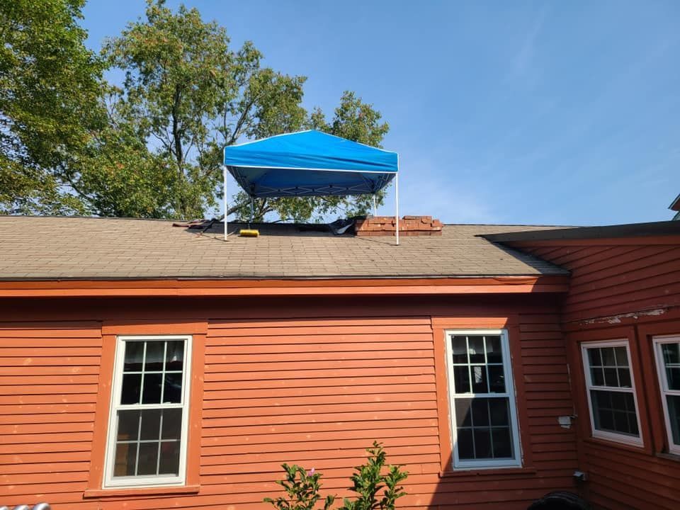 Blue canopy on a red roof, supported by white poles. Orange building, blue sky, green trees.
