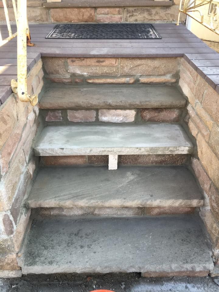 Stone steps leading up to a porch with a dark welcome mat; concrete treads in progress.