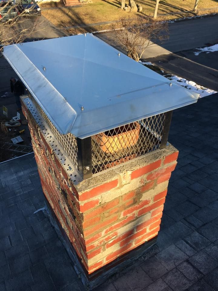 Brick chimney on a dark roof with a metal cap.