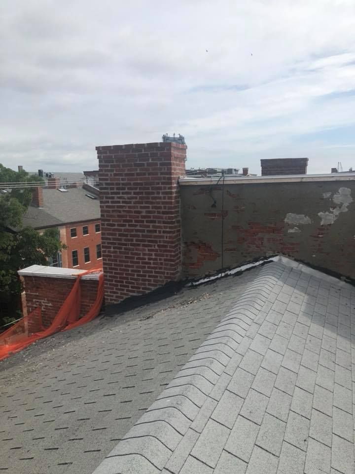 Brick chimney on a gray shingle roof, another chimney in the background. A building with red brick.