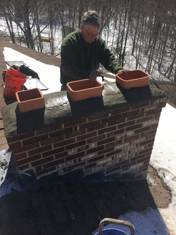 Man on roof placing clay chimney pots. Bricks, snow, and buckets visible.