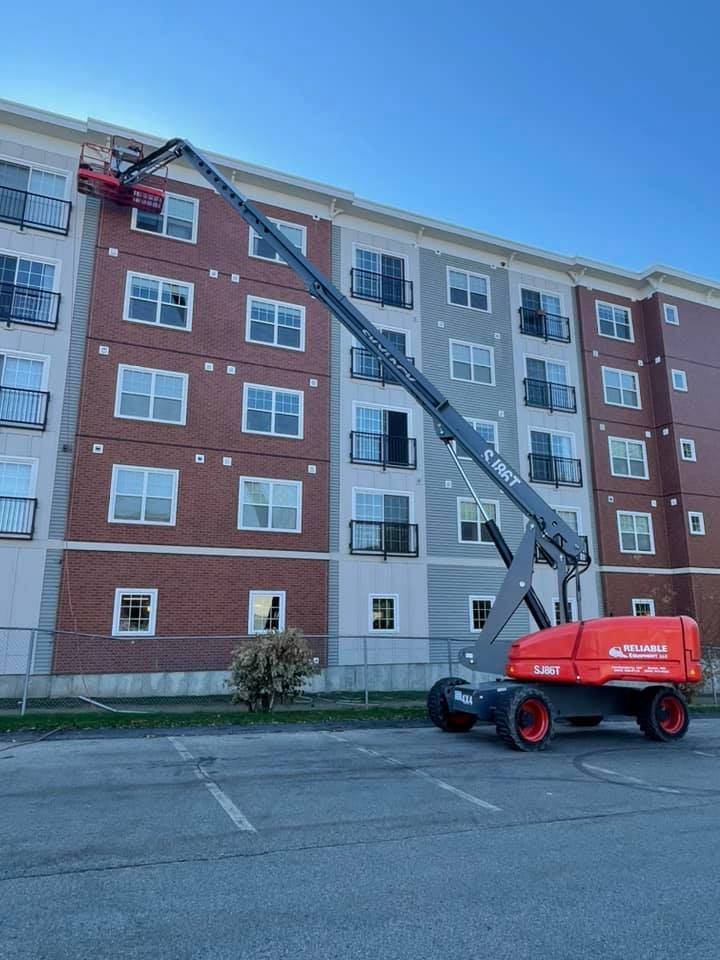 A boom lift reaches up to the side of a multi-story apartment building.