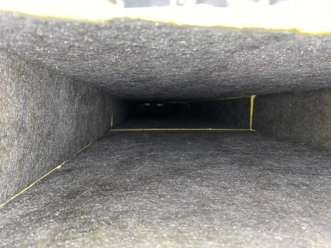 Inside view of a rectangular, dark duct with gray interior insulation, yellow tape along edges, and a distant, shadowy end.