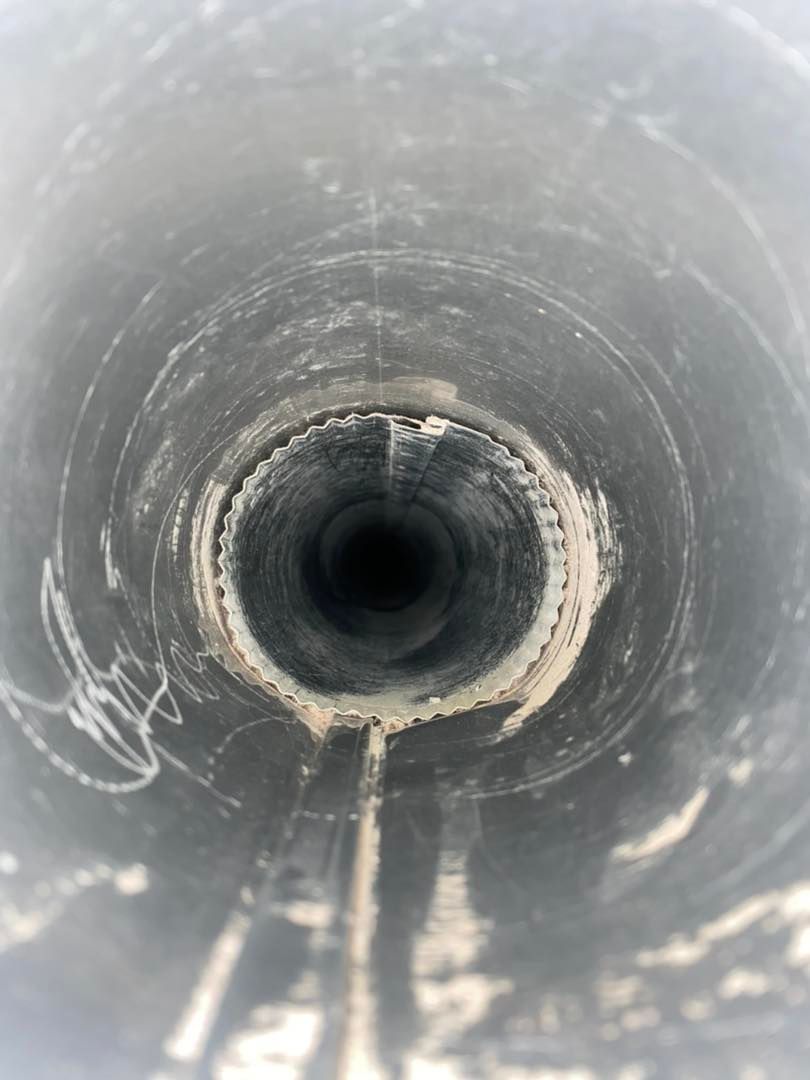 Inside view of a dark pipe, circular and metallic, with white residue around the center opening.