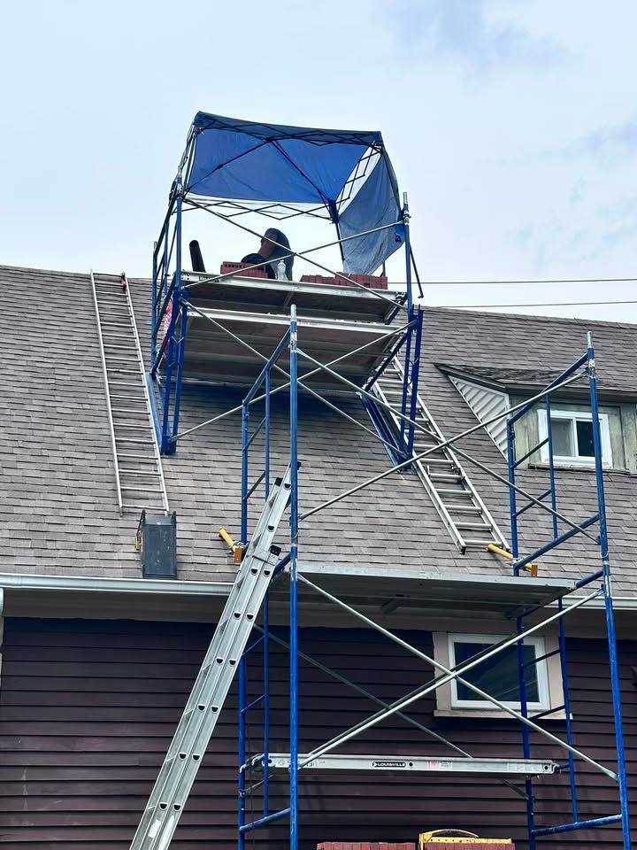 Scaffolding on a roof with a blue canopy, worker, and ladder, presumably for roofing work.