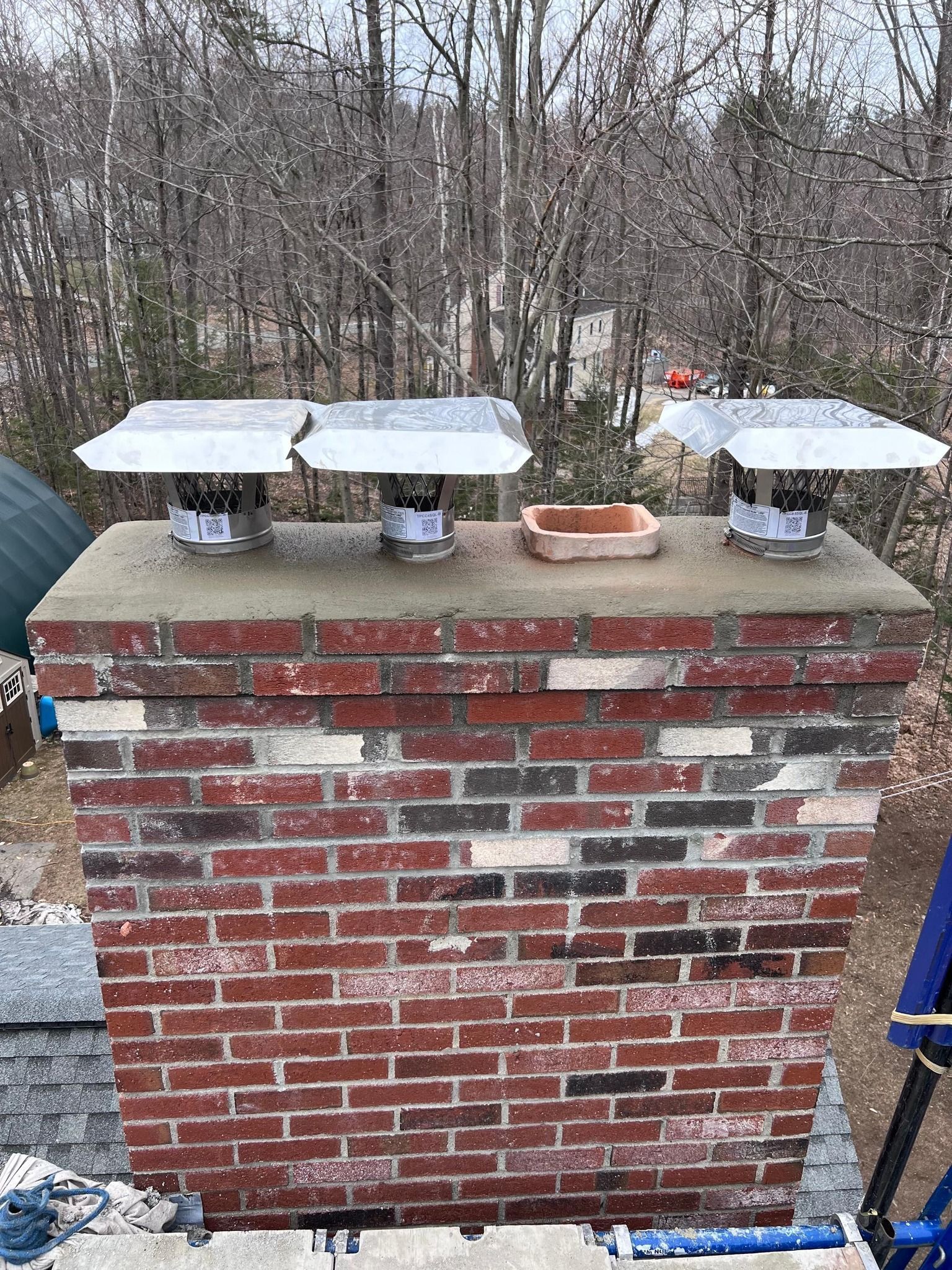 Brick chimney with three metal flue caps and a small rectangular opening on top.