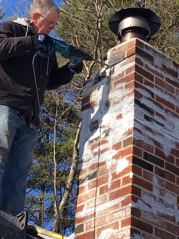 Man drilling into a brick chimney on a sunny day. White paint or residue on bricks.