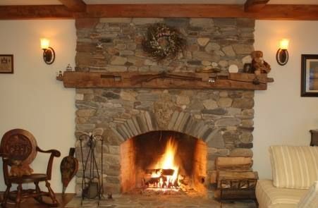 Stone fireplace with roaring fire, wooden mantel, sconces, and a cozy rocking chair.