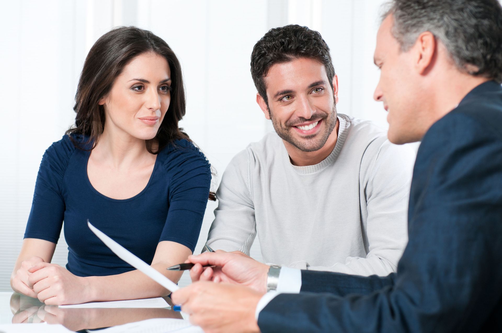 Three people in a meeting, smiling and discussing papers at a table