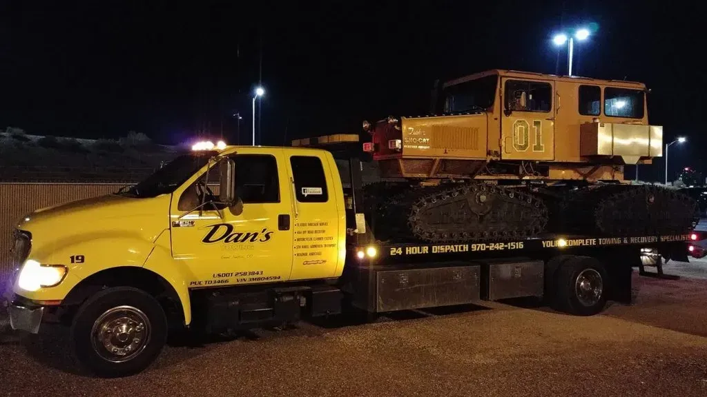 Yellow tow truck hauling a yellow snowcat at night.