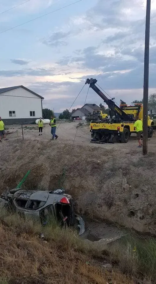 A tow truck pulls a car from a ditch. People in vests stand near the scene.