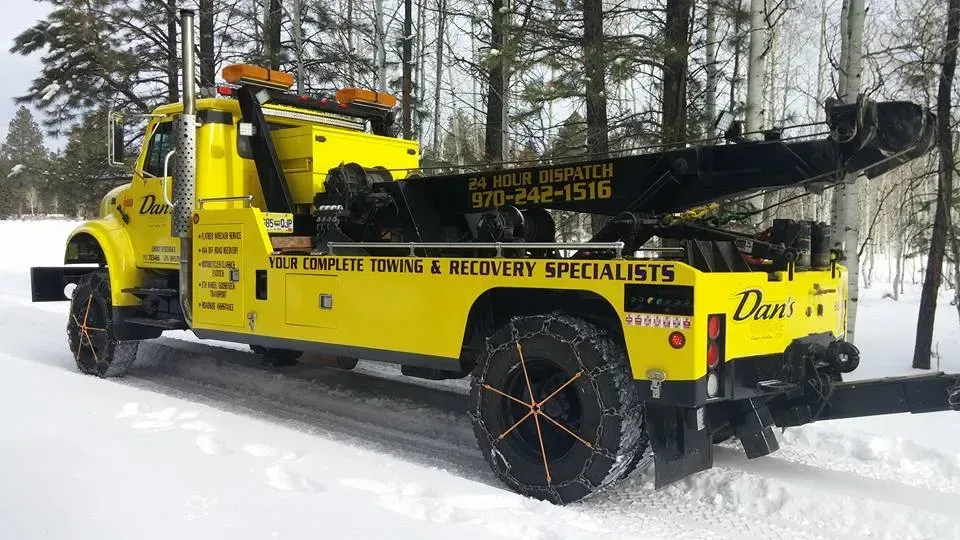 Yellow tow truck with chains on tires driving in snow.