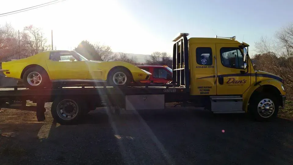 Yellow classic car on a yellow tow truck. Daylight setting.