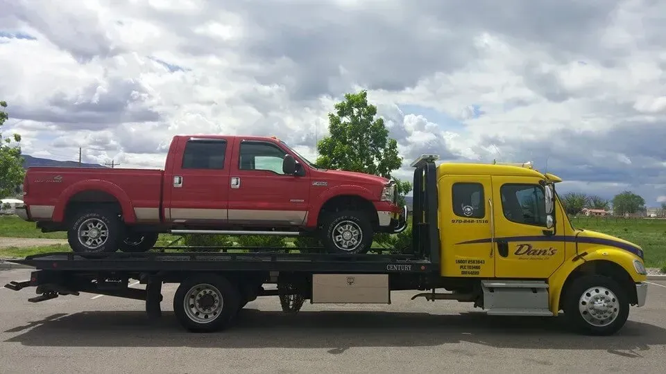 Red pickup truck on a yellow tow truck against a cloudy sky.