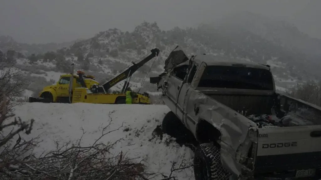 Tow truck pulling damaged Dodge truck from snowy embankment.