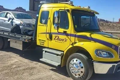 Yellow tow truck with a damaged silver car, roadside.