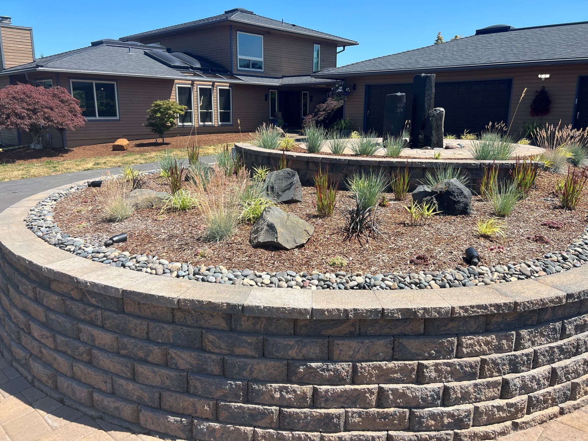Landscaped brick courtyard with circular planter in front of a large house under a blue sky