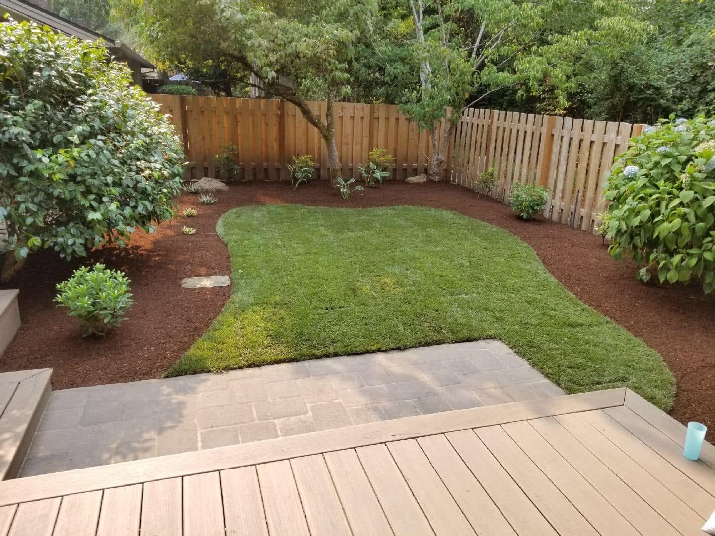 Backyard with green lawn, mulch beds, wooden fence, and a small deck in the foreground