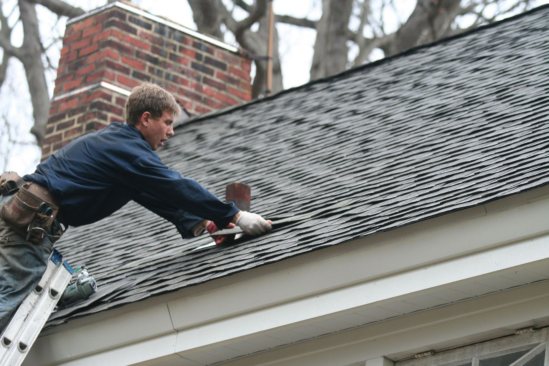 A worker in a cap and dark clothing installs a large, brown corrugated metal roofing sheet on a wooden frame.