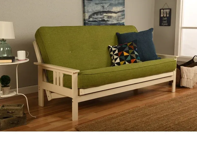 Green futon sofa with cream-colored wooden frame and pillows in a living room setting.