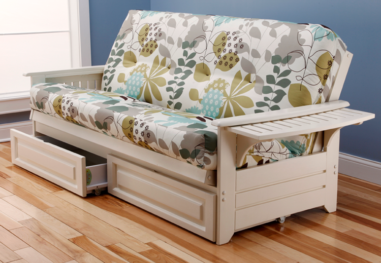 White futon with floral patterned cushions and pull-out drawers, on a wood floor, with a side table.
