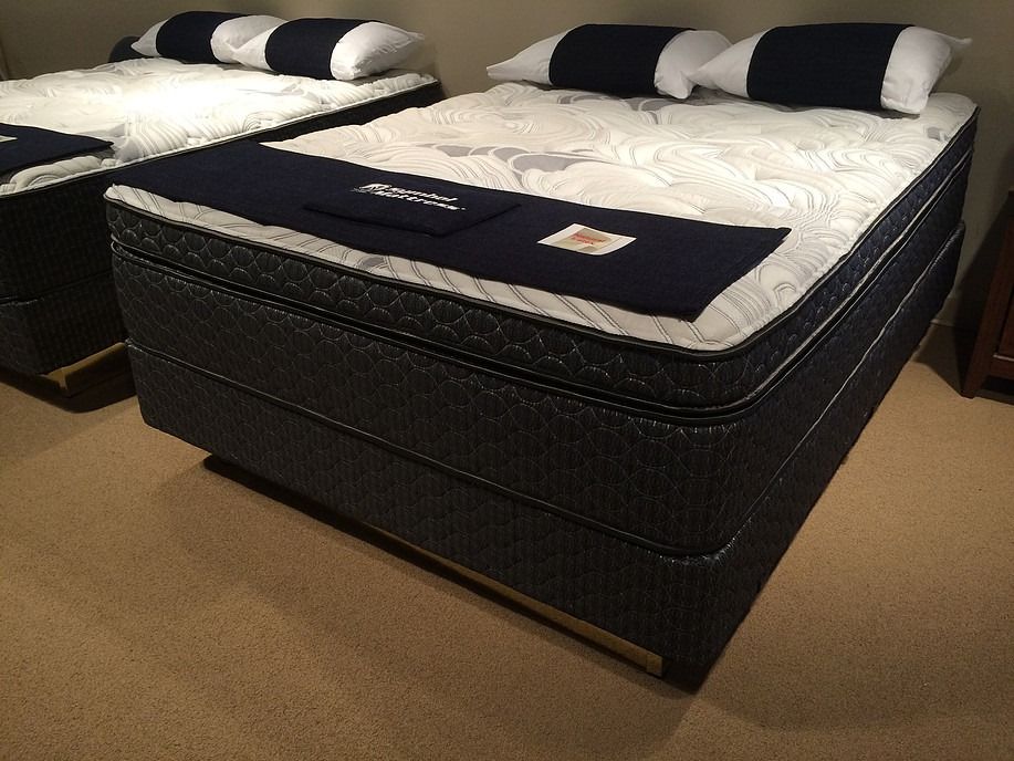 Two blue mattresses with white patterned tops in a room with beige carpet.