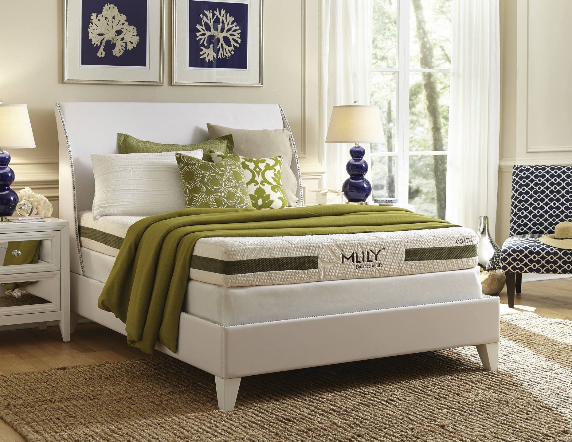 Bedroom with white bed, patterned chair, art, and lamps. Green accents and rug.